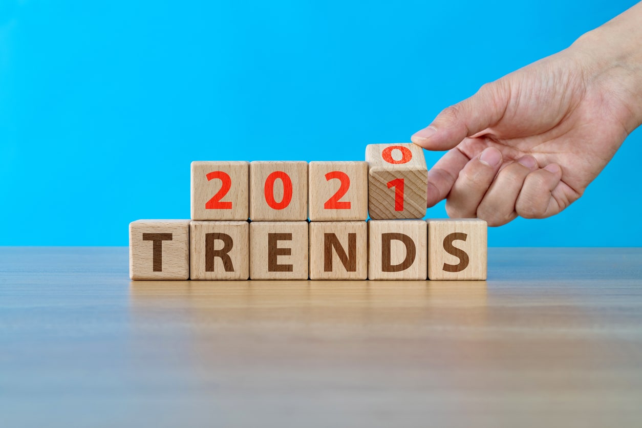 Wooden Blocks With a Blue Background, Spelling Out "2021 Trends" With a Hand Flipping Over a Block